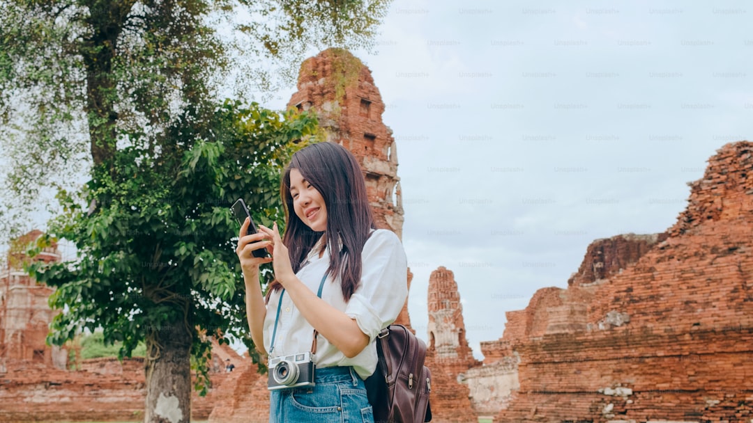Cheerful beautiful young Asian backpacker blogger woman casual with camera look at photo on smartphone smile with happy 