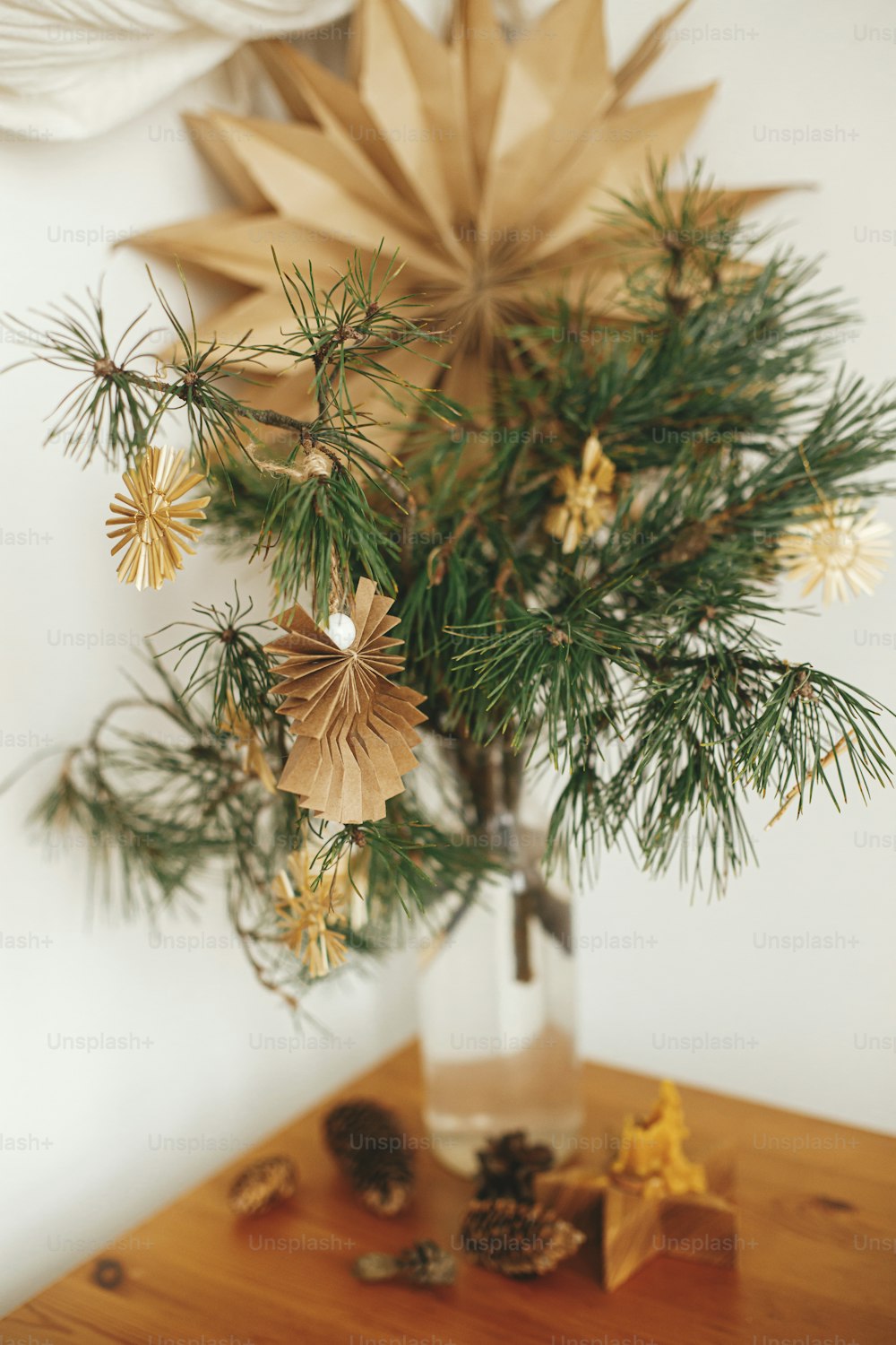 Stylish christmas star straw ornaments and paper angel on pine branches on table in vase on background sweden star. Festive decorated scandinavian room. Eco plastic free decorations