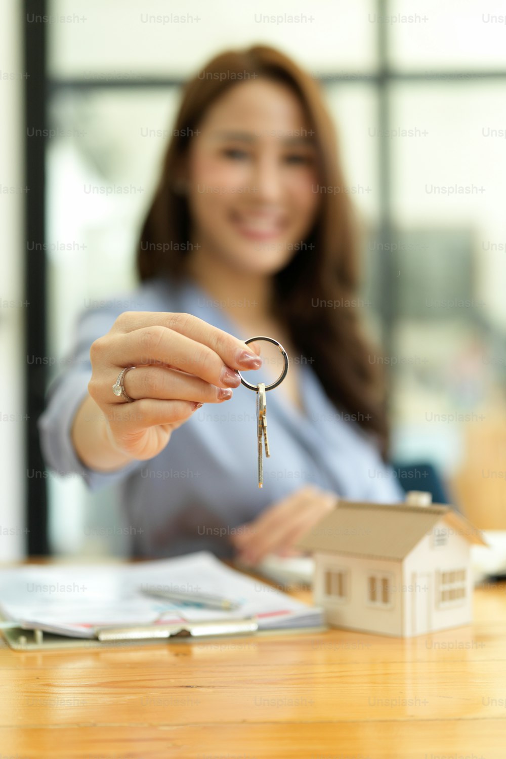 Manos enfocadas, hermoso agente inmobiliario que sostiene la llave de la casa, el modelo de la casa y el contrato de alquiler sobre la mesa