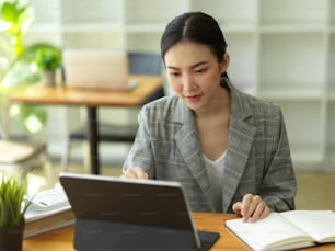 ポータブルタブレットコンピュータで作業する若い女性ビジネスウーマン。机に座り、キーボードで入力する女性サラリーマン