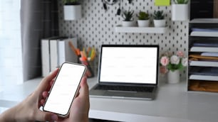 Man hands holding smart phone with white screen and sitting in home office.