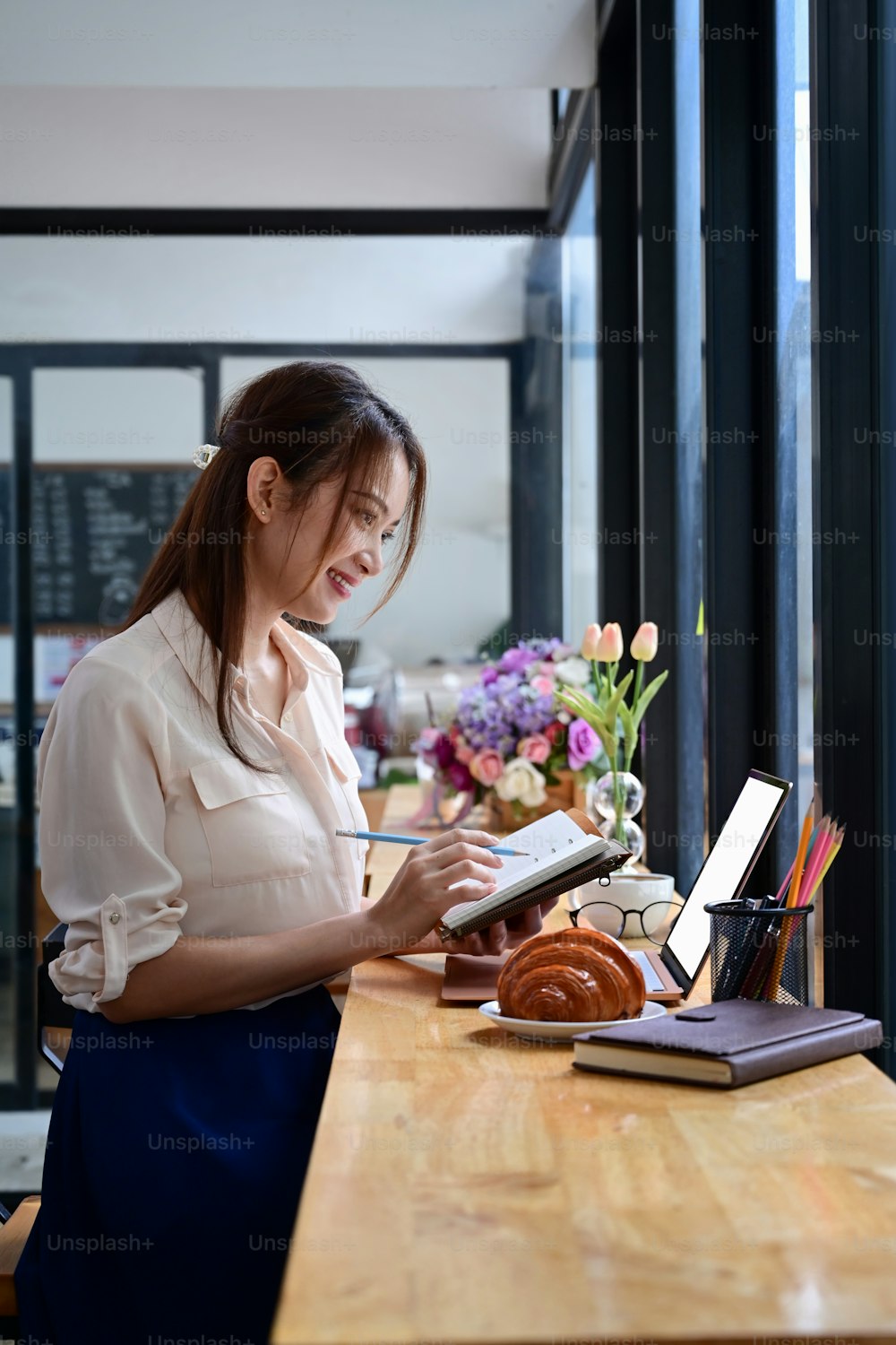 Seitenansicht lächelnde junge Frau, die in der Nähe des Fensters im Café sitzt und einen Laptop benutzt.