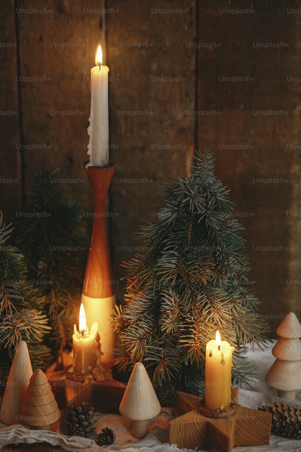 クリスマスのアドベント。夜のスカンジナビアの部屋の素朴な古い木製の背景にスタイリッシュな燃えるクリスマスキャンドル、松の木、コーンのモダンな装飾。大気モーメント