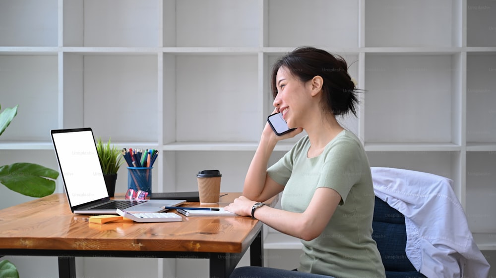 Smiling woman entrepreneur talking on mobile phone and working with laptop computer.