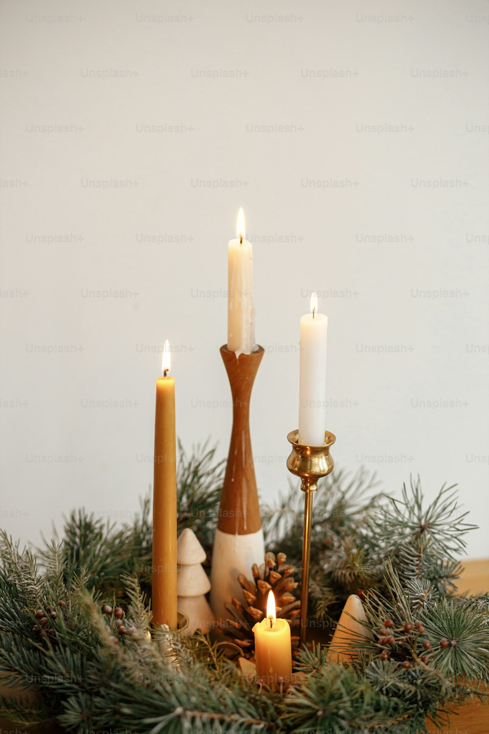Elegante ghirlanda di natale con candele e decorazioni di pini su tavolo di legno sullo sfondo della parete bianca nella moderna stanza festiva. Atmosferico periodo invernale. Festa dell'Avvento