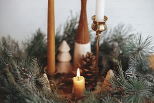 Weihnachtsadvent. Stilvolle Kerzen, die im Weihnachtskranz brennen, schließen sich mit Tannenzapfen und Baumdekor auf einem Holztisch auf dem Hintergrund der weißen Wand im festlichen Raum an. Stimmungsvolle Winterferienzeit