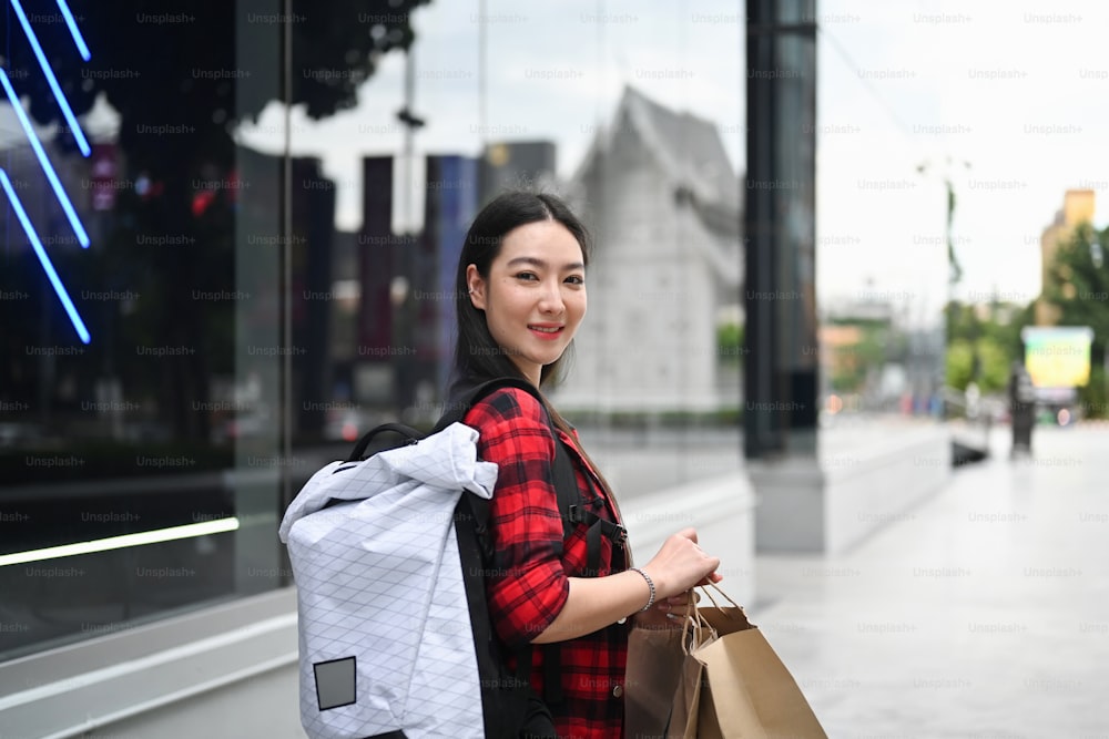 Smiling young Asian woman holding shopping bags and walking at outdoor shopping mall.