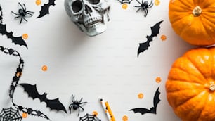 Happy Halloween holiday concept. Halloween decorations, bats, spiders, skull, pumpkins on white table. Flat lay, top view.