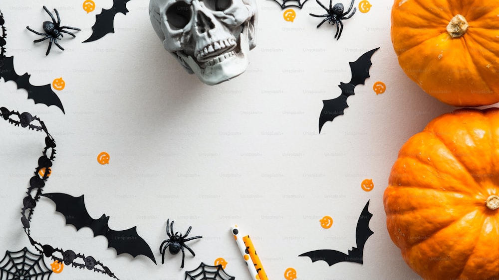 Happy Halloween holiday concept. Halloween decorations, bats, spiders, skull, pumpkins on white table. Flat lay, top view.