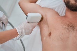 Cropped photo of a Caucasian man undergoing an underarm laser hair removal in a wellness center