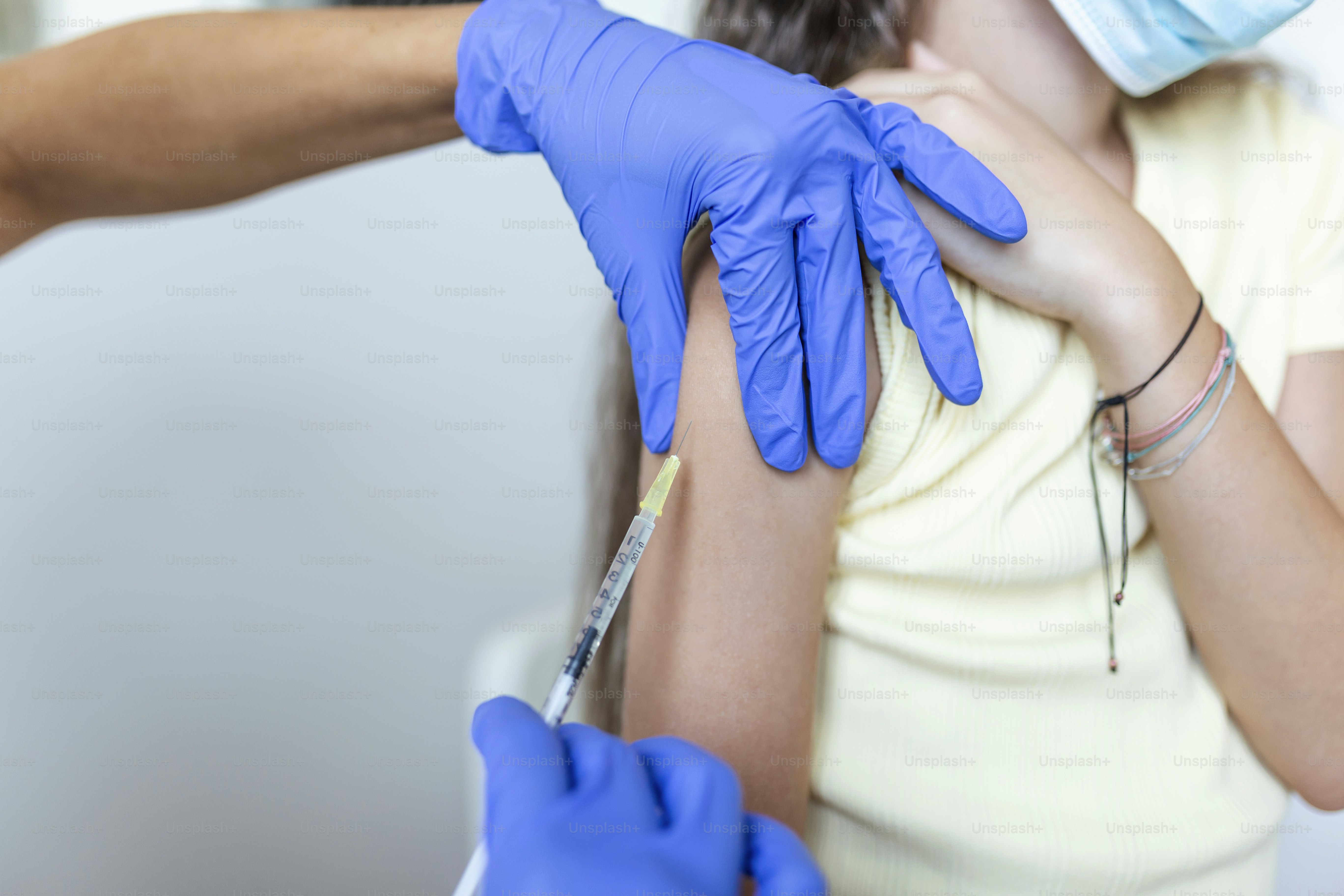 Doctor vaccinating girl. Injecting COVID-19 vaccine into patient's arm. Girl in medical masks getting vaccinated against covid-19, doctor giving injection of coronavirus vaccine at hospital.