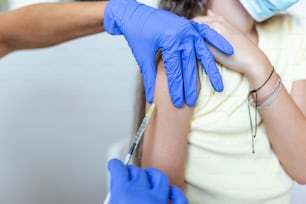 女の子に予防接種をする医者。COVID-19ワクチンを患者の腕に注射する。covid-19の予防接種を受ける医療用マスクの女の子、病院でコロナウイルスワクチンを注射する医師。