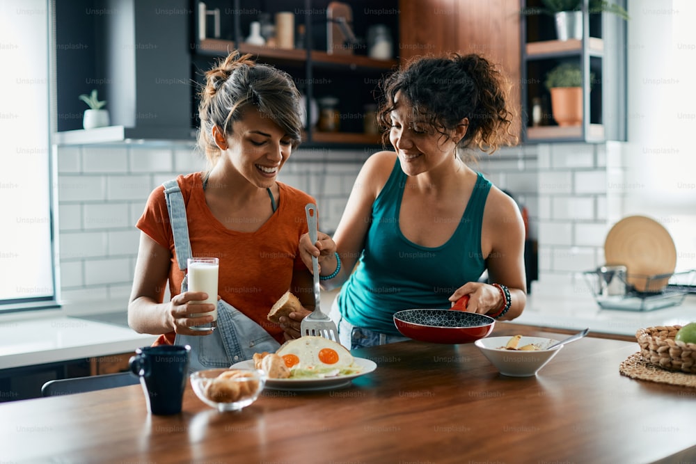 Happy lesbian woman serving breakfast to her girlfriend at dining table in the kitchen.