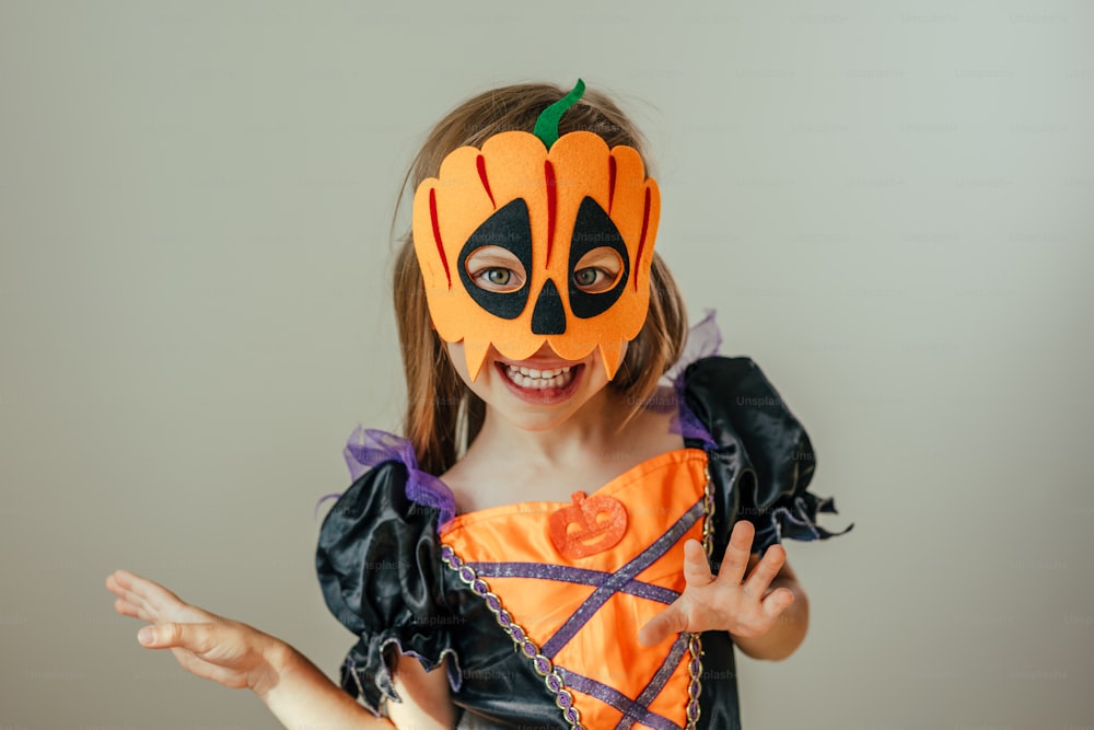 Porträt eines kleinen Mädchens mit Halloween Hexenkostüm und Kürbismaske drinnen. Selektiver Fokus.