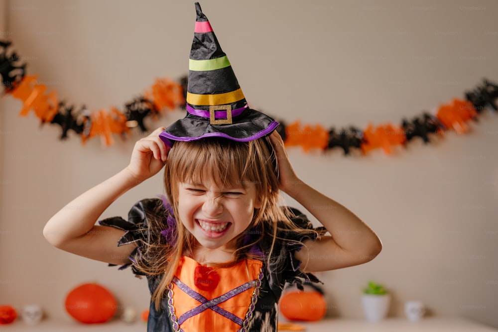 Portrait of little girl dressed Halloween witch costume and hat in decorated room. Selective focus on the face.