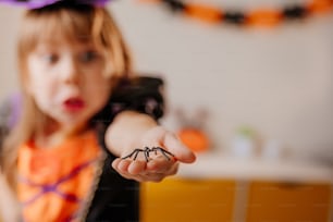Menina vestida fantasia de bruxa de Halloween segurando aranha de brinquedo na mão. Foco seletivo na aranha. Emoção do medo.