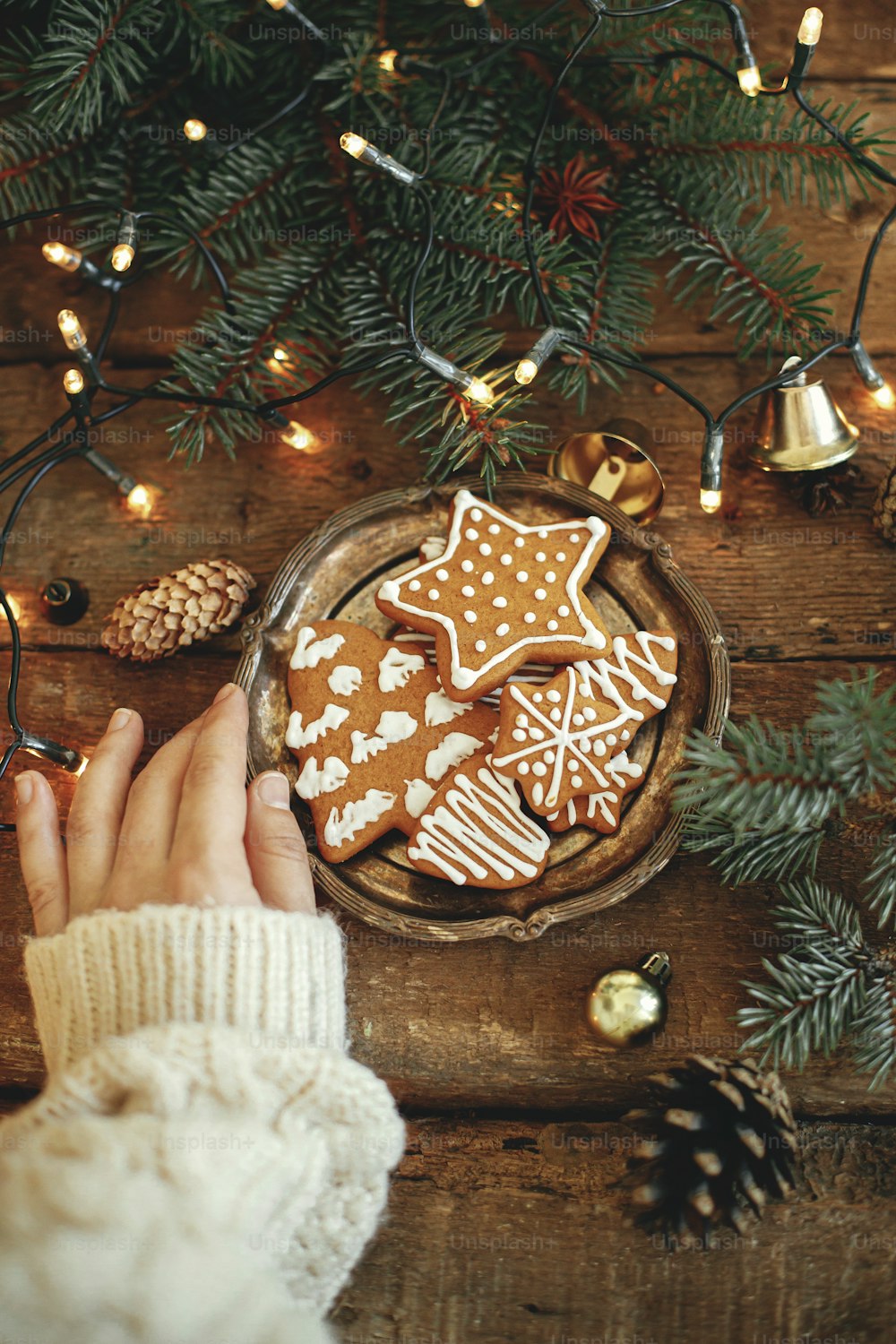 Piatto a mano con biscotti di pan di zenzero di Natale, rami di abete, luci calde su tavolo di legno rustico, flat lay. Immagine invernale atmosferica. Buone feste. Deliziosi biscotti fatti in casa