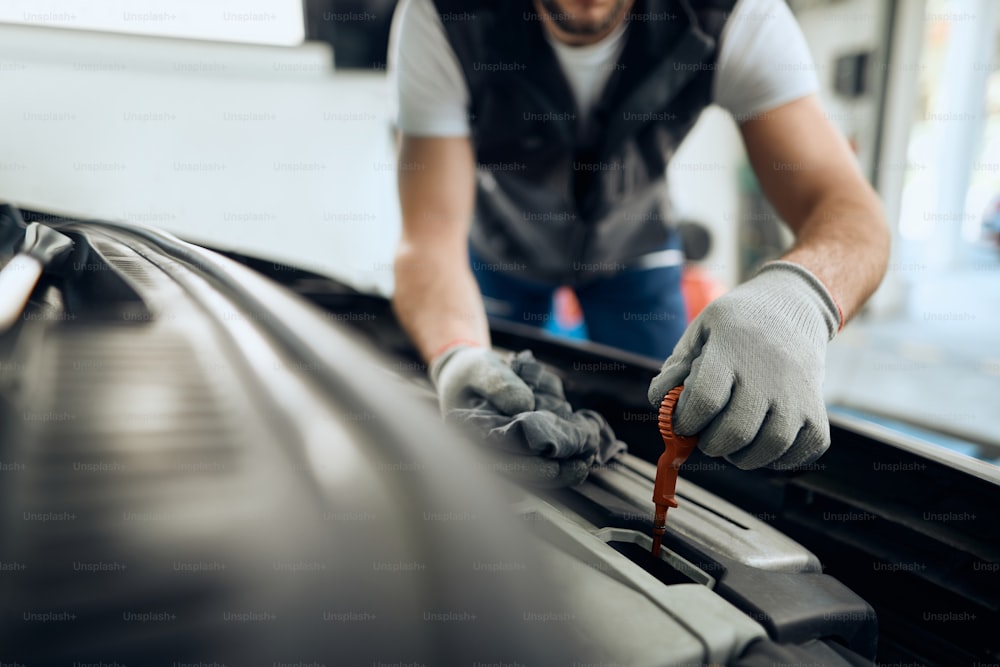 Close-up do reparador de automóveis verificando o nível de óleo durante a manutenção do motor em uma oficina.