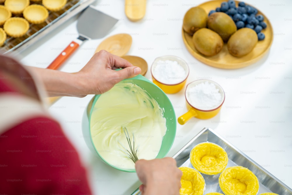 Asian woman bakery shop owner preparing bakery in the kitchen. Adult female making whipping cream cheese from fresh milk on the table. Small business entrepreneur and indoor activity lifestyle baking concept.