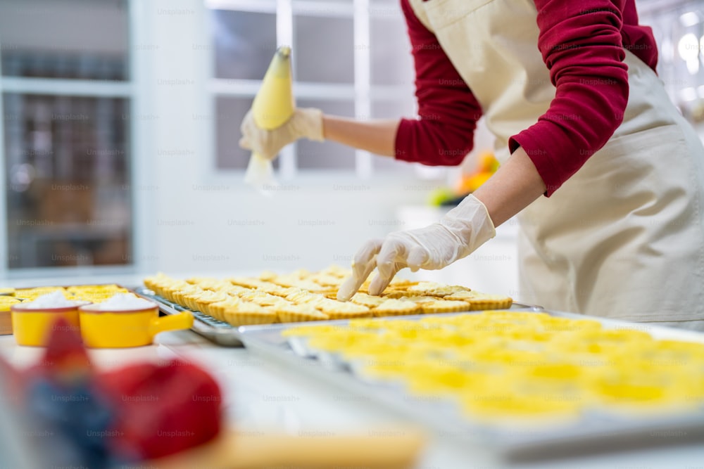 부엌에서 빵집을 준비하는 아시아 여성 빵집 주인. 테이블에 과일 타르트를 만들기 위해 타르트 반죽을 굽는 여성 제빵사. 소기업 기업가 및 실내 활동 라이프 스타일 개념.