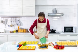 Asiatische Bäckereibesitzerin bereitet Bäckerei in der Küche vor. Erwachsene Frau, die Frischkäse aus frischer Milch auf dem Tisch schlägt. Kleinunternehmer und Indoor-Aktivitäts-Lifestyle-Backkonzept.