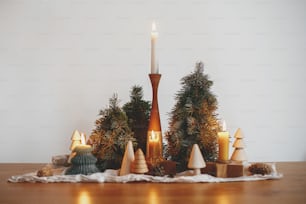 Eleganti candele di natale e decorazioni di pini su tavolo di legno sullo sfondo della parete bianca nella moderna sala festiva scandinava. Atmosferico periodo invernale. Festa dell'Avvento
