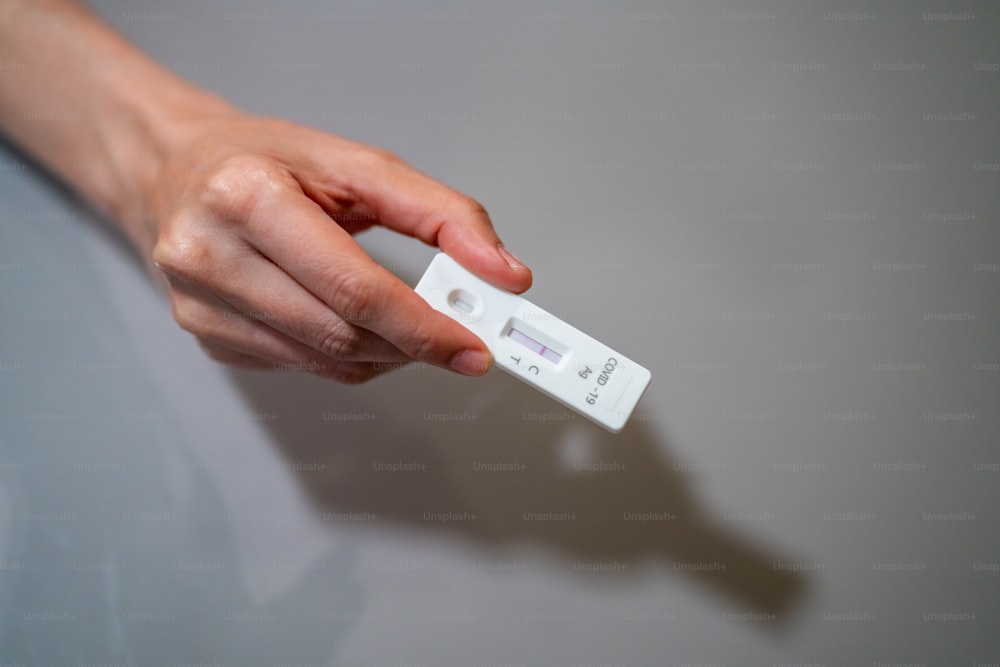Une femme asiatique utilise un kit de test antigénique rapide pour l’autotest de l’épidémie de COVID-19 à la maison. Femme adulte présentant des résultats négatifs de COVID-19 sur une bandelette de test. Concept de protection contre la pandémie de coronavirus COVID-19.