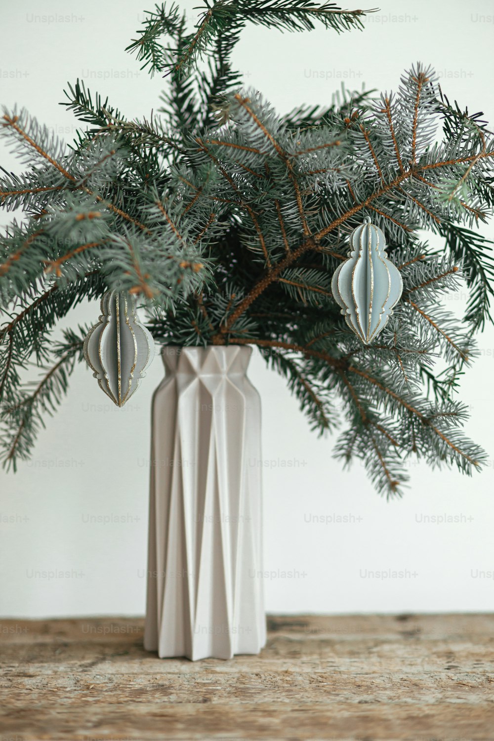 Stilvoller Weihnachtsschmuck auf Tannenzweig in moderner Vase Nahaufnahme. Moderne Holzkugel auf Ast auf weißem Hintergrund. Festliche einfache und kreative Einrichtung im skandinavischen Zimmer. Frohe Weihnachten!