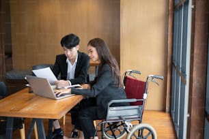 Femme handicapée en fauteuil roulant travaillant sur un nouveau projet d’entreprise avec son collègue au bureau.