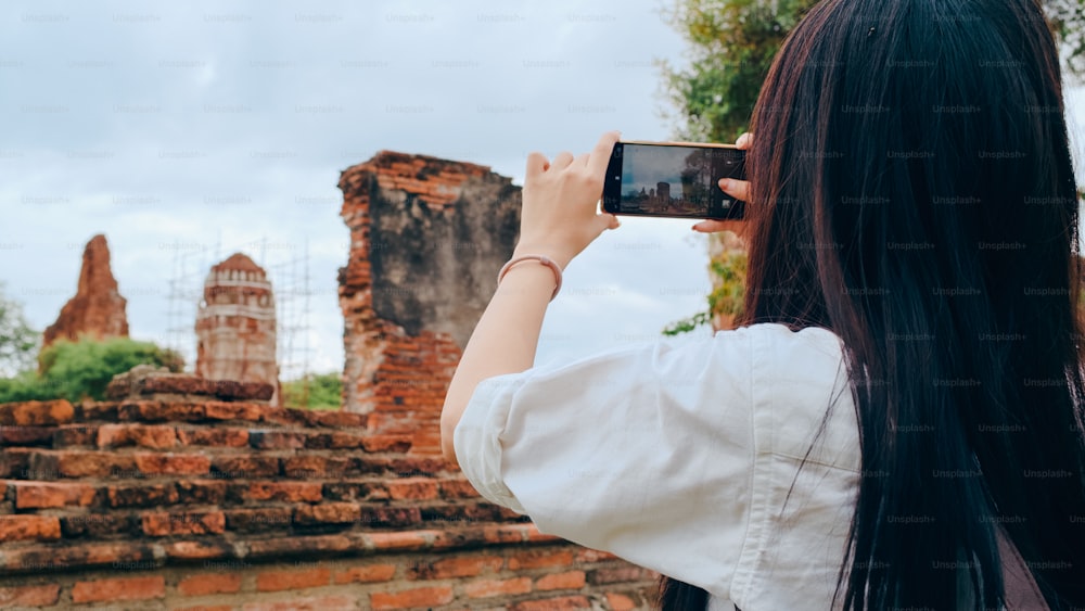 Donna asiatica viaggiatrice che utilizza lo smartphone per scattare una foto mentre trascorre un viaggio di vacanza ad Ayutthaya, Thailandia, turista giapponese si gode il suo viaggio in un incredibile punto di riferimento nella città tradizionale.