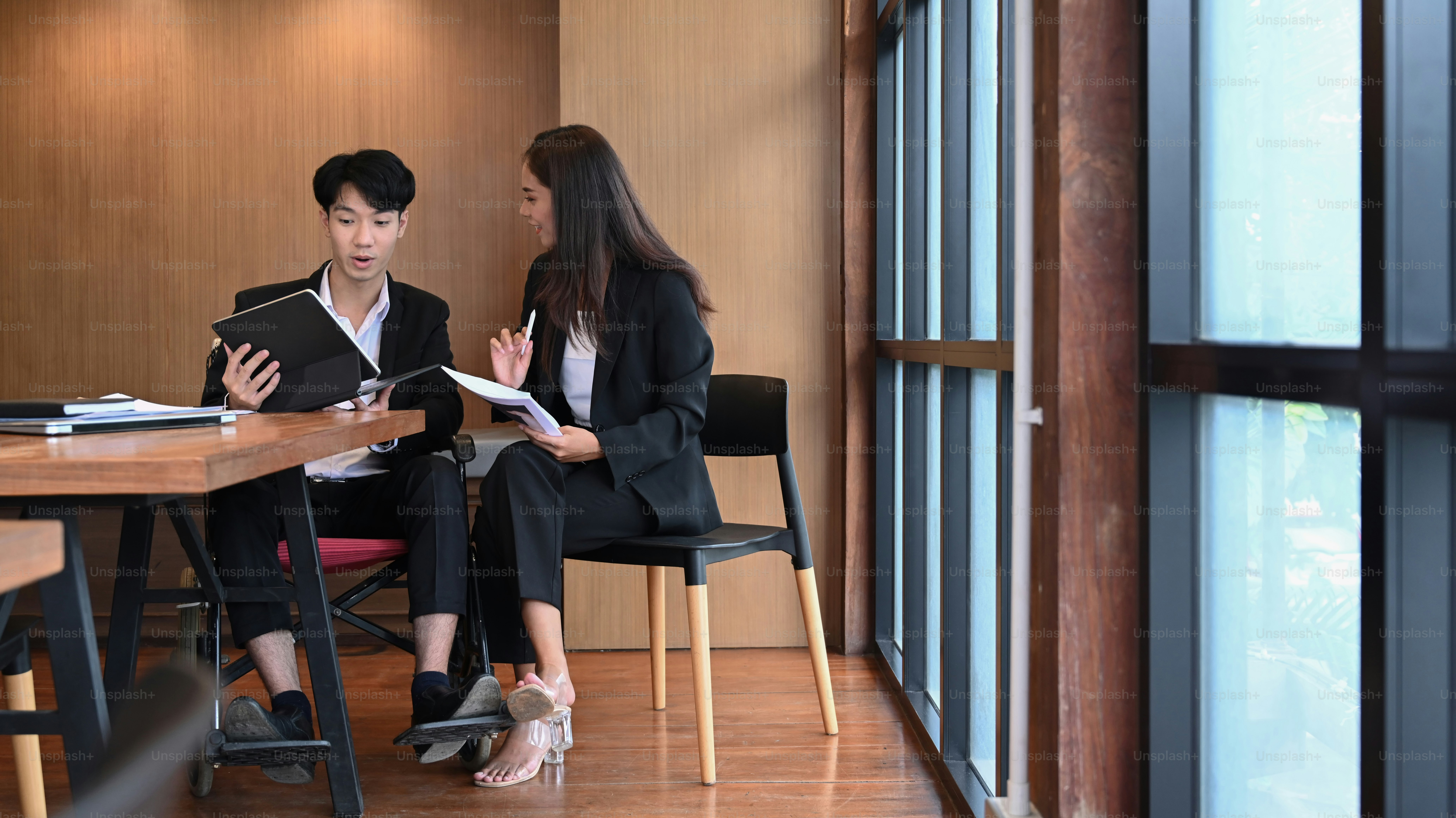 Disabled young man on wheelchair working in modern office with his colleague.