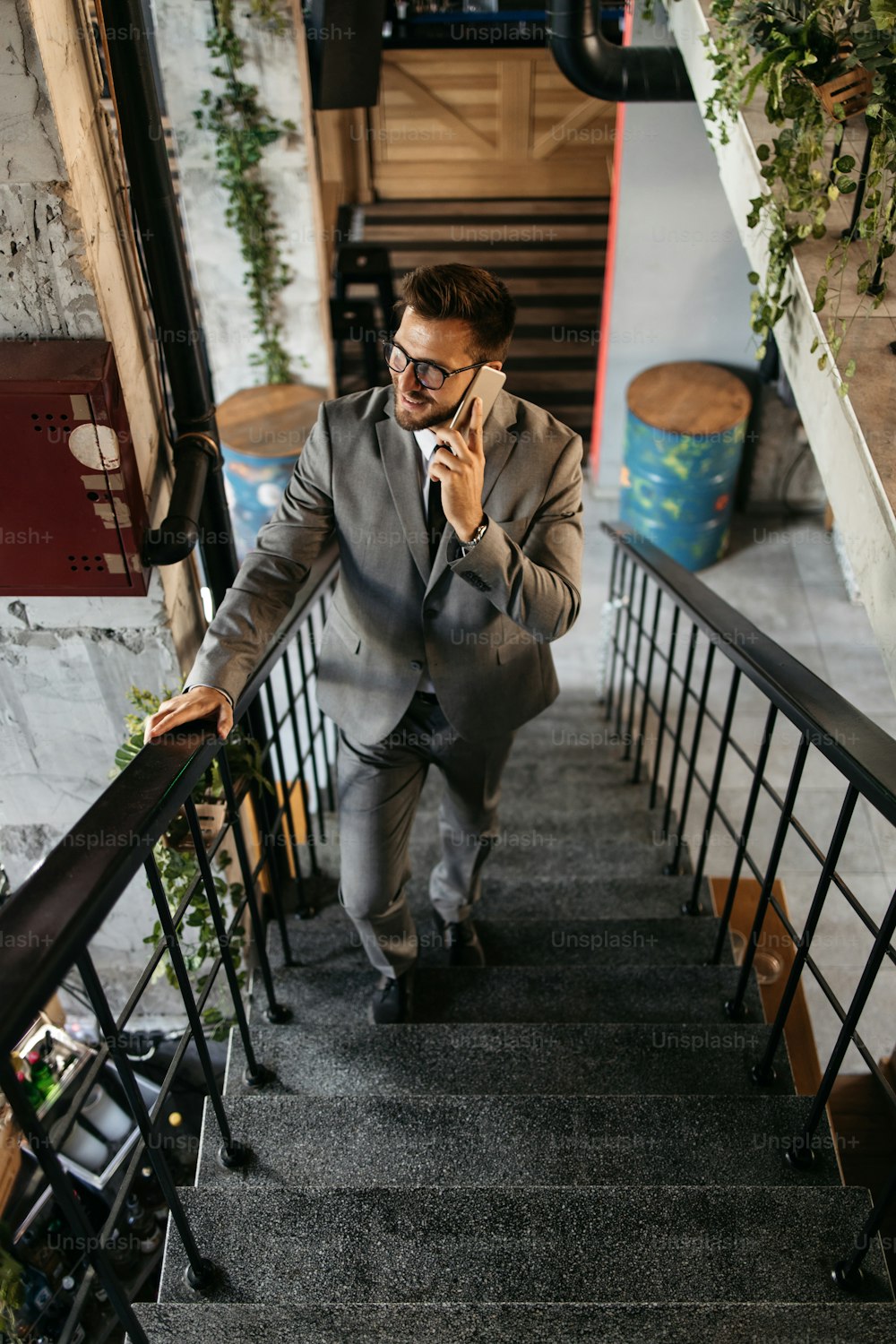 Handsome middle age businessman standing in modern restaurant and using his smart phone to talk with someone. He is positive and happy.