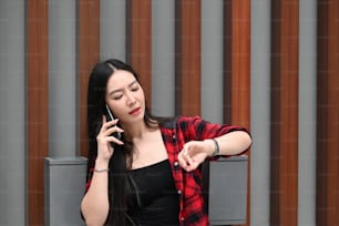Young Asian woman talking on mobile phone and checking time on her wrist watch.