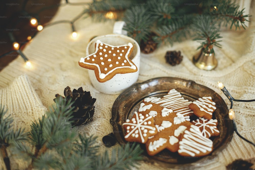 Galleta de jengibre de estrella de Navidad en taza de café caliente, ramas de abeto, adornos, galletas y luces cálidas sobre fondo de punto acogedor. Tiempo festivo atmosférico y casa hygge. Felices Fiestas
