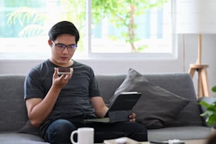 Young man talking on speaker phone and using laptop computer in living room.