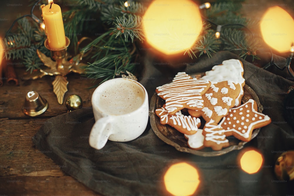 Biscoitos de gengibre de Natal, café em elegante xícara branca, galhos de abeto, luzes quentes no guardanapo e mesa de madeira rústica. Imagem atmosférica. Hygge campo de inverno. Boas Festas!