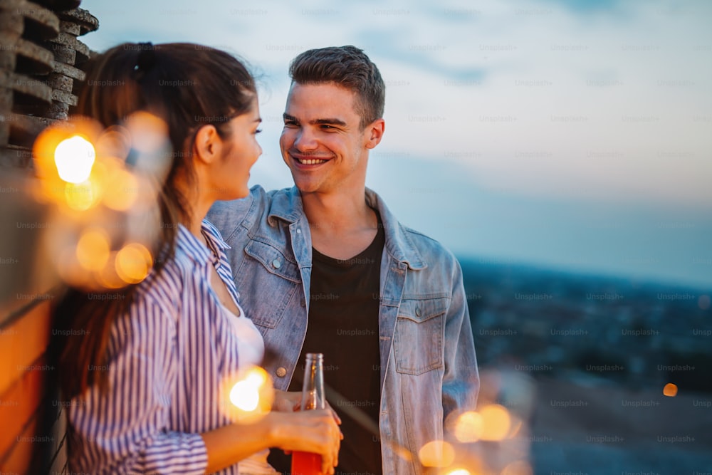 Jovem casal feliz no amor se divertindo na festa no telhado ao pôr do sol.