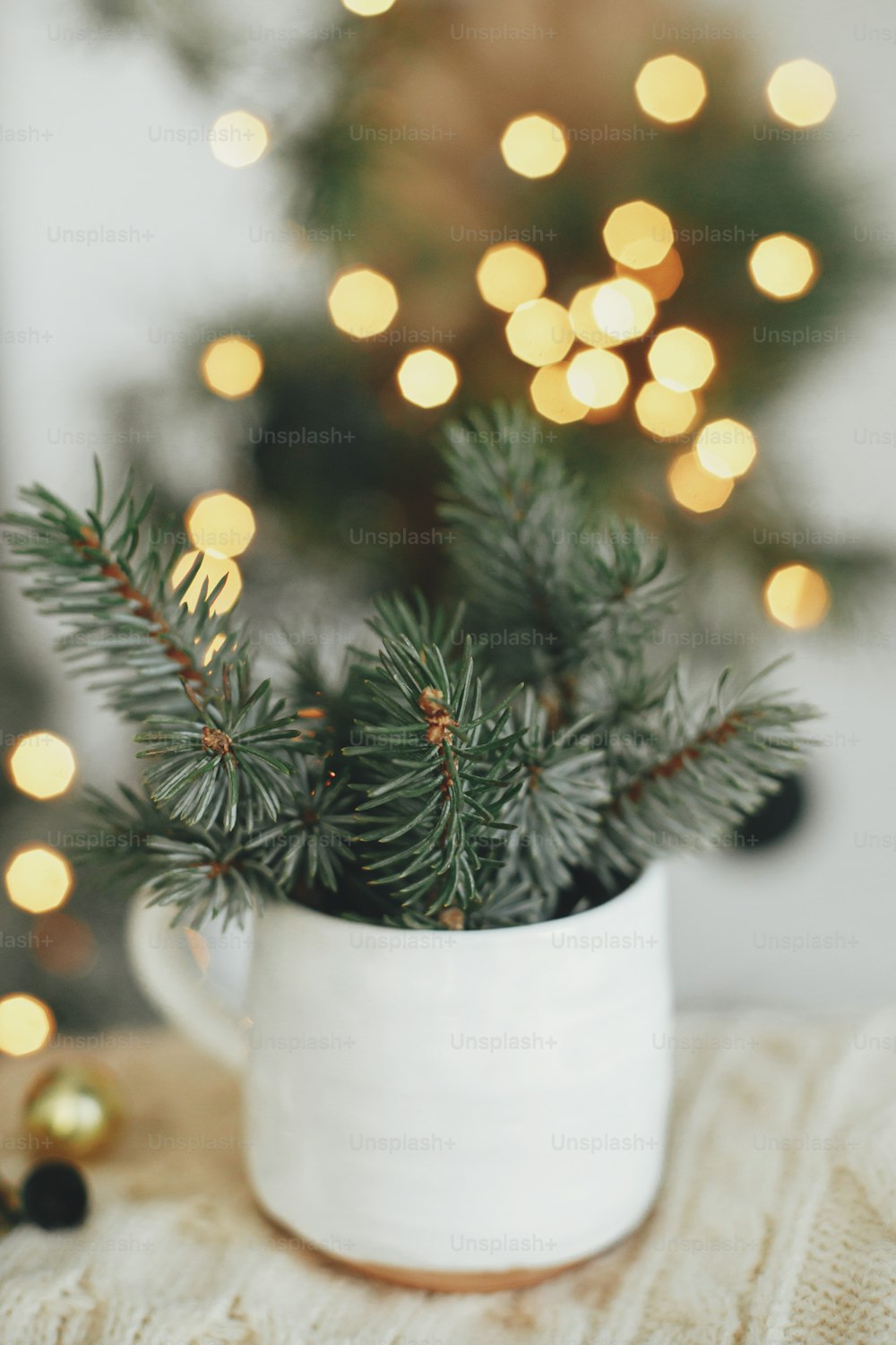 Atmospheric hygge home. Merry Christmas! Stylish cup with fir branches on cozy sweater on background of warm lights in festive scandinavian room. Magic winter time. Happy Holidays!
