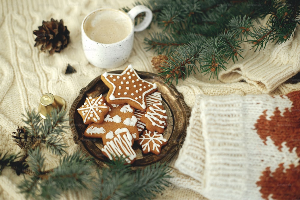 Homemade christmas gingerbread cookies, warm coffee in stylish cup and fir branches on background of cozy knitted sweater or blanket. Atmospheric winter time. Hygge. Happy Holidays