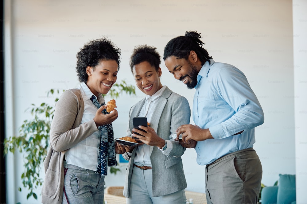 Happy African American businesswoman and her colleagues using smart phone while taking a break from work in the office.