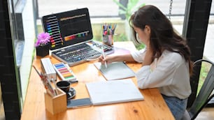 Artista femenina que dibuja el diseño de la imagen en la tableta digital antes de dibujar en el póster de la lona en el estudio, materiales para colorear en la mesa de madera