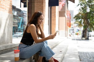 Smiling Asian woman sitting on stairs using smart phone.