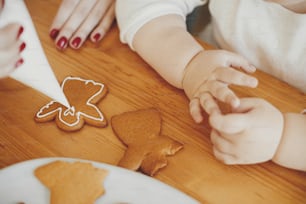 Linda hija y madre decorando galletas de jengibre navideñas con glaseado en una mesa de madera, de cerca. Tiempo en familia juntos, preparativos para las vacaciones de Navidad. Momento auténtico de mamá hija