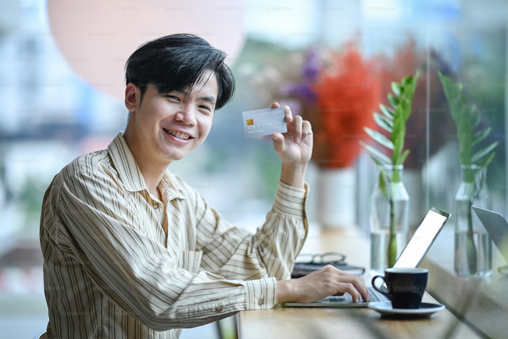 Young Asian man holding credit card and smiling to camera.