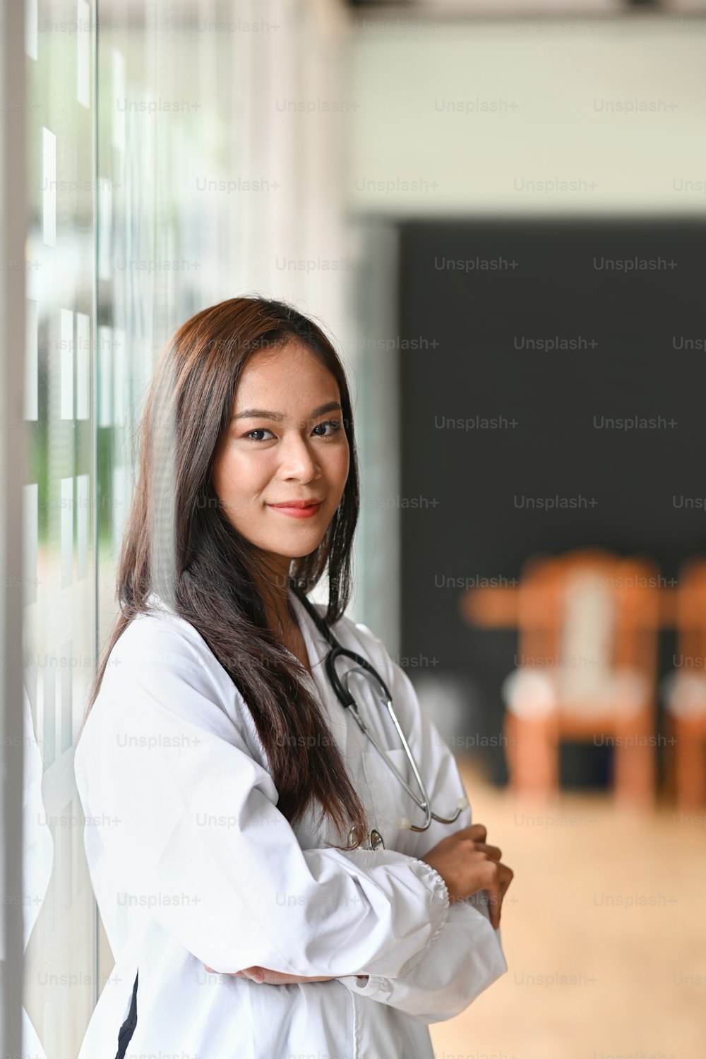 Beautiful female doctor in white uniform standing with crossed arms and smiling to camera.
