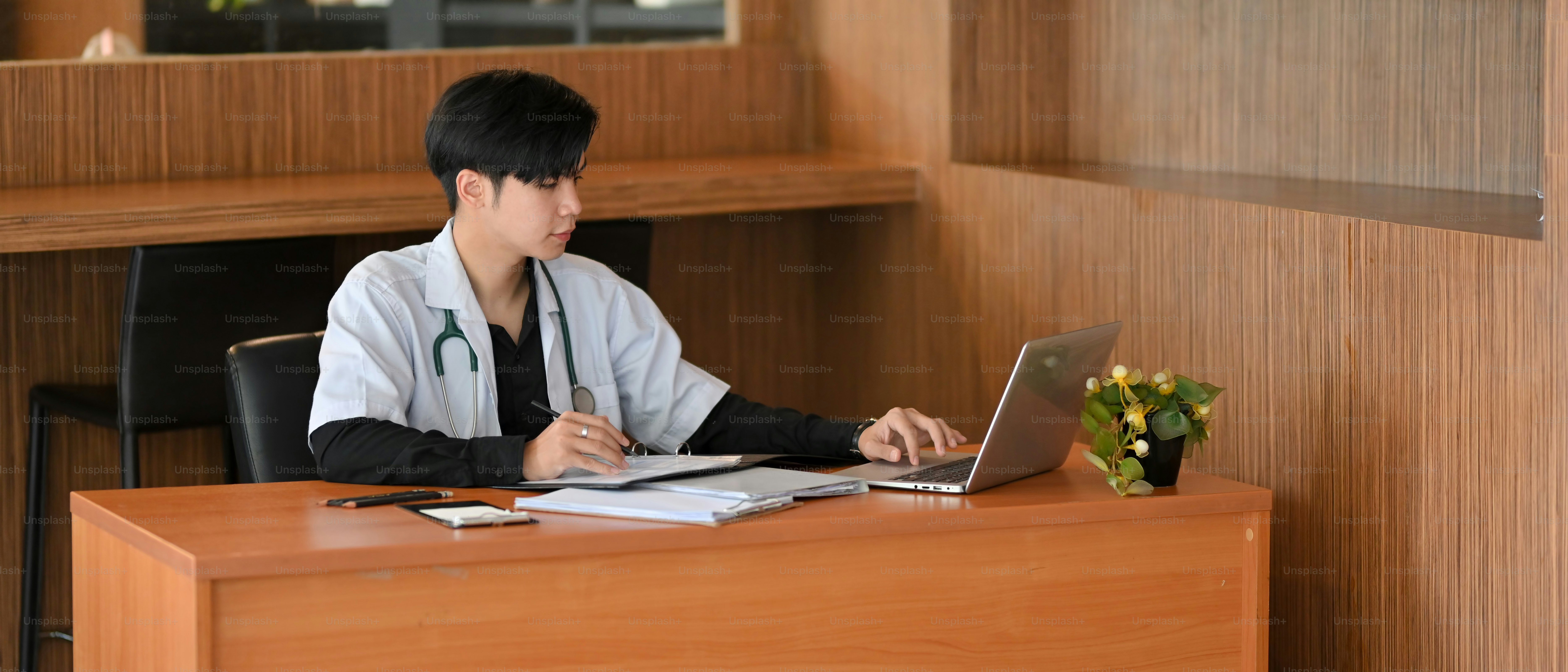 An Asian doctor sits at his desk works on laptop computer, examining the patient's medical history in preparation for an examination and diagnosis