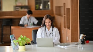 Bella dottoressa asiatica che lavora sul laptop in ufficio, facendo follow-up online con il paziente per la situazione pandemica
