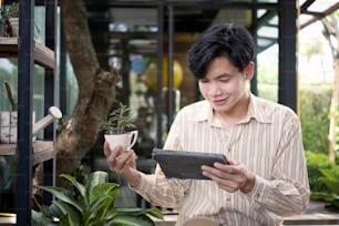 Man small business entrepreneur using digital tablet and holding potted plant.
