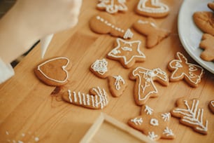 Decorating christmas gingerbread cookies with icing on wooden table close up. Hands decorating baked christmas cookies with sugar frosting. Xmas holiday preparations, atmospheric time