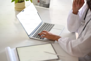 Closeup, Doctor typing on laptop keyboard, laptop and tablet in blank screen mockup. searching medical research, online consultation